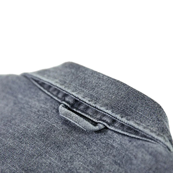Close-up of a blue washed denim overshirt, focusing on the collar and a small loop detail just below the collar seam. The natural cotton fabric has a textured, slightly faded appearance.
