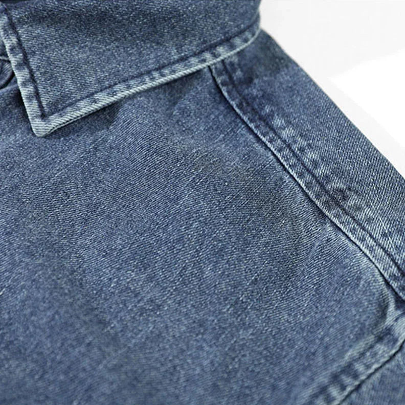 Close-up view of a blue washed denim overshirt, focusing on the collar and shoulder seam with visible stitching and natural cotton texture.