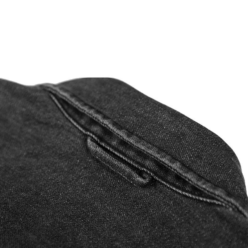 Close-up view of a hidden pocket sewn into a black overshirt, showing the subtle opening and fine stitching detail on the natural cotton fabric.