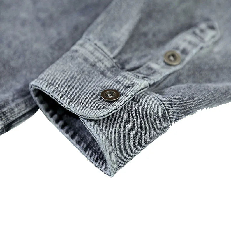Close-up of a gray washed denim overshirt cuff with two metal buttons, highlighting the texture and stitching details of natural cotton. The background is white.