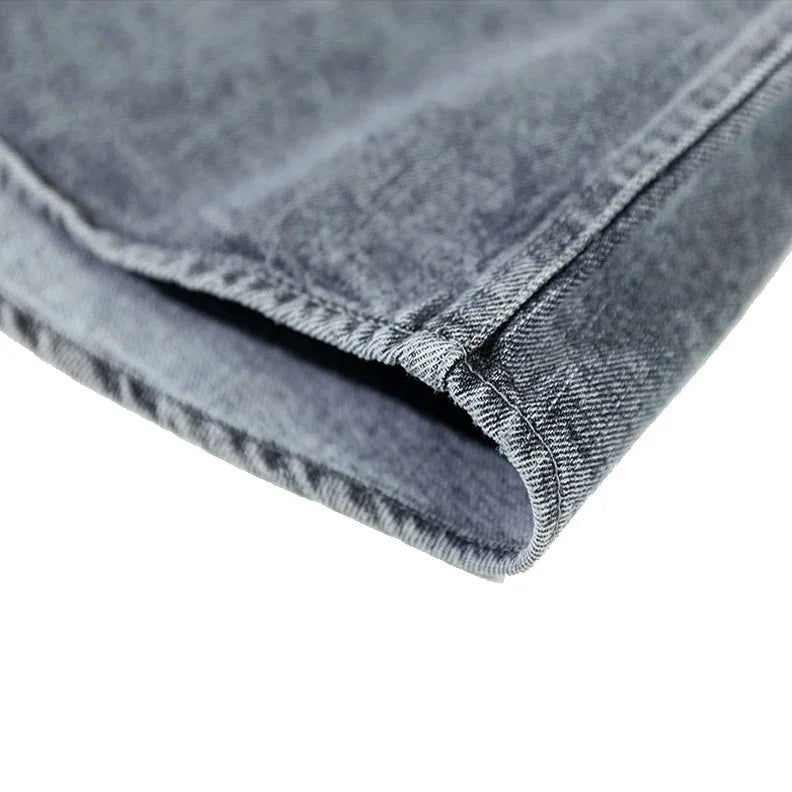 Close-up of the hem of a pair of blue washed denim jeans, showing the fabric texture, stitching, and neatly finished edge against a white background.