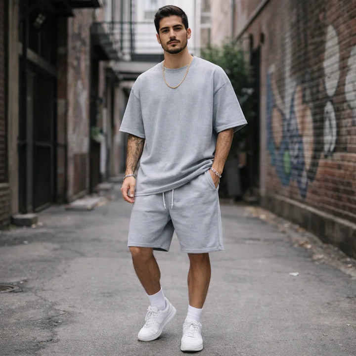 Man in gray casual shorts set and sneakers standing in urban alleyway, Rovelli style