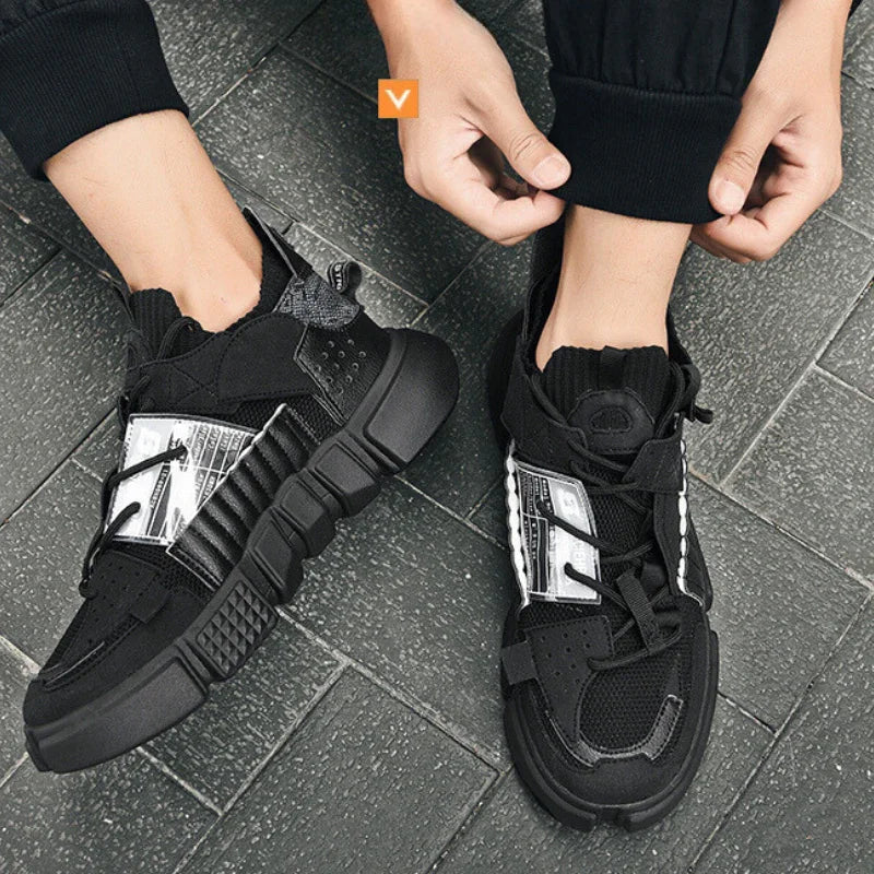 A person wearing black and white Extreme VS7 Sneakers with thick soles, adjusting the cuff of their black pants while standing on a gray tiled floor.