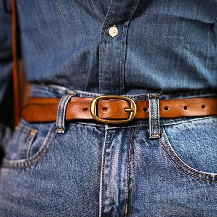 A close-up of a person wearing a blue denim shirt tucked into blue jeans, secured with a genuine leather belt featuring a gold buckle for a touch of Southern style.