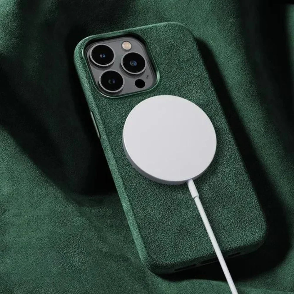 A smartphone with a green case featuring a suede finish is lying on a green fabric surface, with a circular wireless charger attached to its back and a charging cable connected.