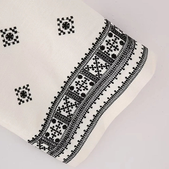 White fabric with intricate black embroidery features geometric and floral patterns along the edge and small square motifs—ideal for crafting boho chic pants or stylish wide-leg trousers.