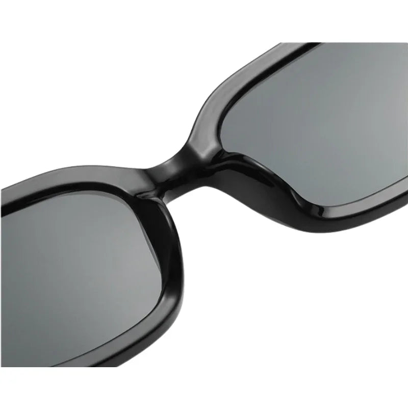 Close-up view of the bridge and lenses of black, rectangular designer sunglasses featuring dark tinted lenses and UV400 protection.