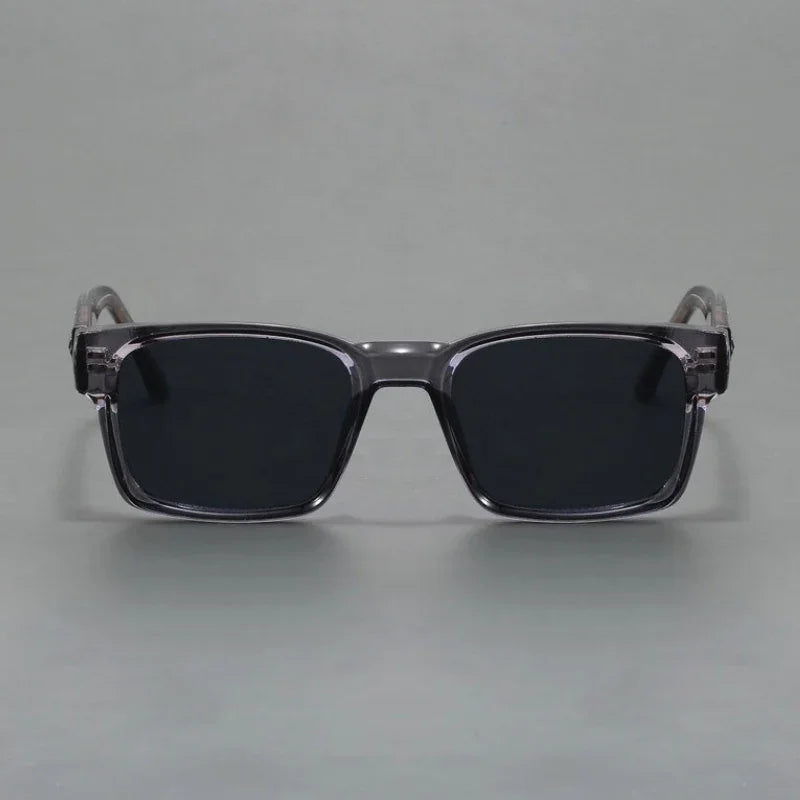 A pair of rectangular, black sunglasses with thick, translucent gray frames and modern design, offering UV400 protection, displayed against a plain gray background.