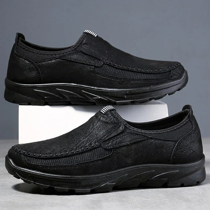 A pair of black Men Leather Casual Shoes with textured soles and stitched detailing, displayed with one shoe on a white box and the other in front, offering a comfortable fit for any occasion against a gray background.