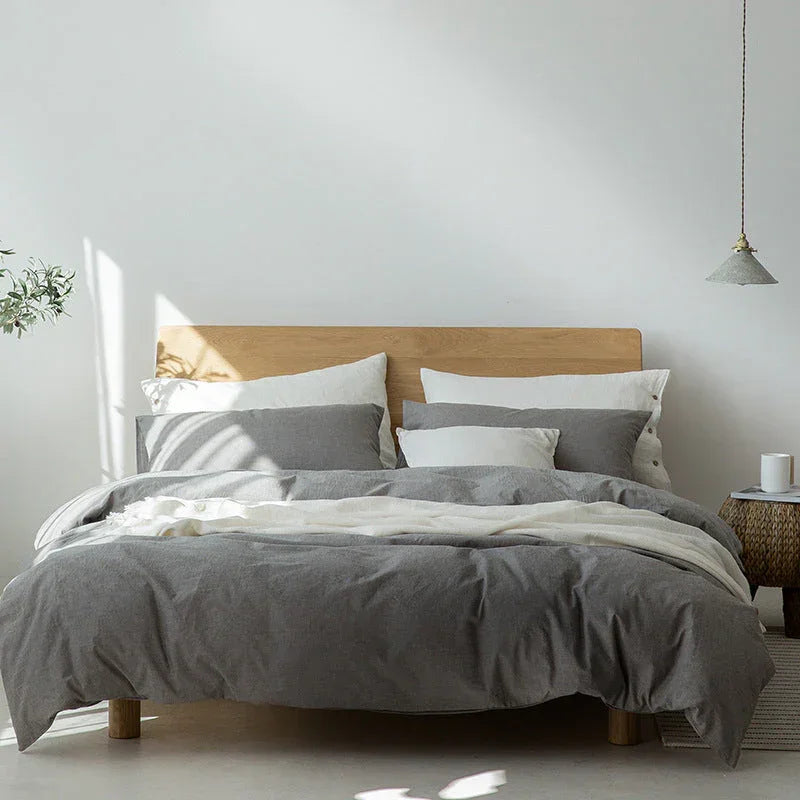 Modern minimalist bedroom with gray and white bedding, wooden headboard, and natural light