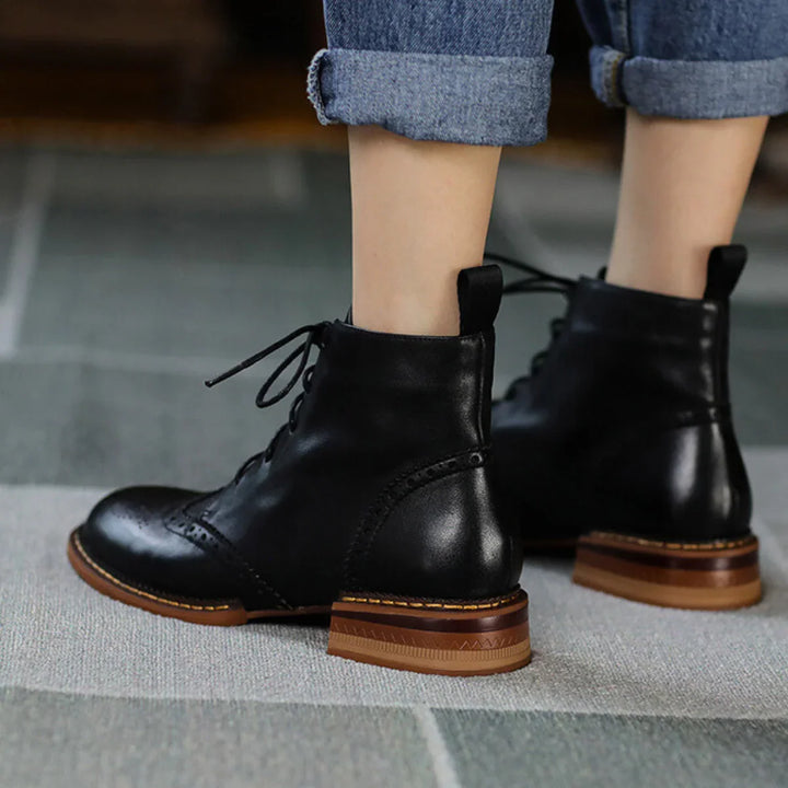 A true urban trendsetter stands on a patterned rug, showcasing genuine leather brogue boots with brown heels and rolled-up blue jeans. The photo, taken from behind, highlights the stylish footwear.