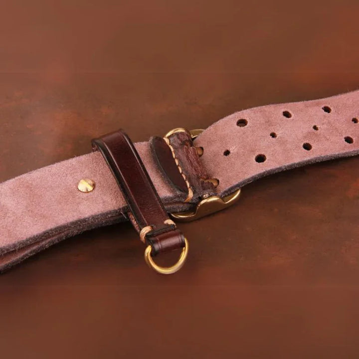 Close-up of a vintage leather belt with gold-colored metal buckle and ring, showing detailed stitching and multiple adjustment holes on a rustic brown background.