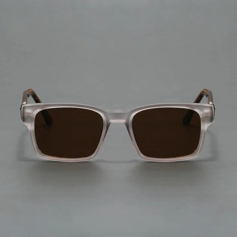 A pair of square, transparent-framed sunglasses with a modern design and dark tinted lenses offering UV400 protection, displayed against a plain gray background.