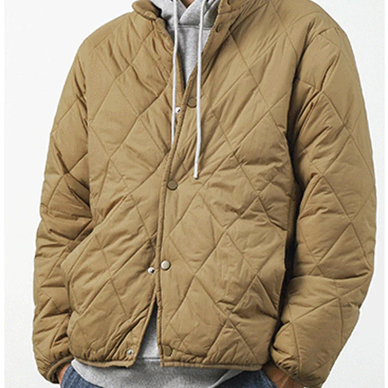 A person wearing a tan, diamond-stitched padded jacket over a gray hoodie with white drawstrings, standing against a plain light background.