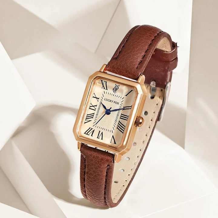 A rectangular face watch with a white dial, black Roman numerals, blue hands, and a genuine leather strap is displayed on a geometric white background.