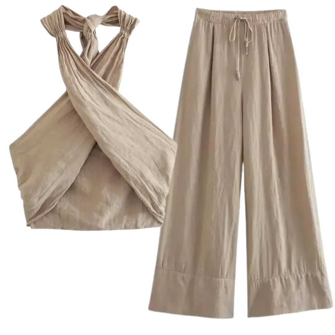 A beige two-piece outfit for effortless summer style, featuring a chic halter collar on the sleeveless, criss-cross top and wide-leg pants with a drawstring waist, both crafted from lightweight, textured fabric.