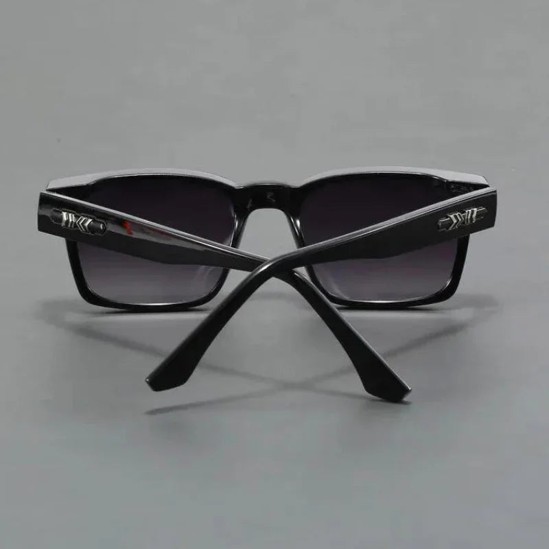 A pair of black sunglasses with dark lenses, shown from the back with the arms crossed. The durable frames feature metallic decorative details near the hinges. The background is a plain gray surface.