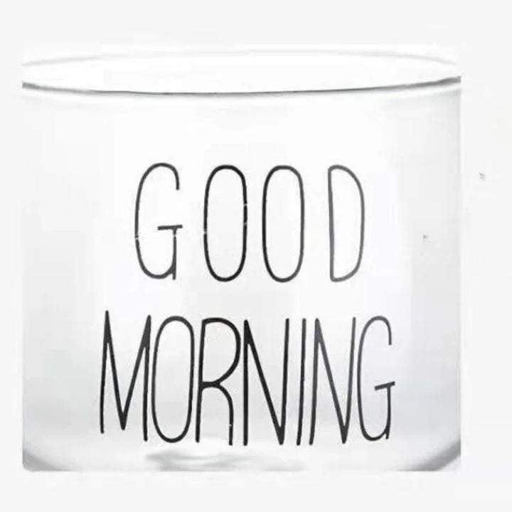 A transparent glass cup with a clear design and the words GOOD MORNING printed in bold, black letters on its side.