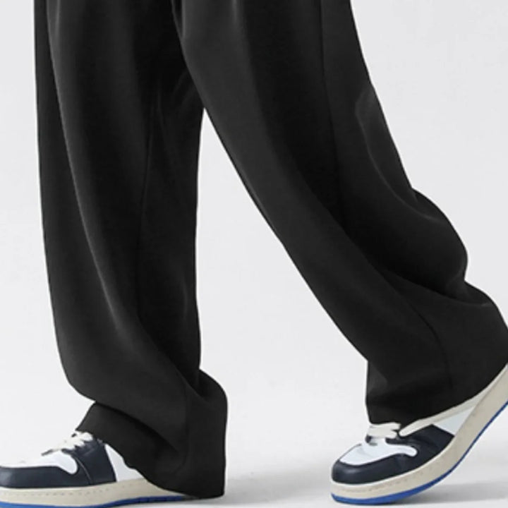 A person wearing loose-fitting streetwear joggers and blue-and-white sneakers stands on a light-colored floor. Only the lower legs and feet are visible.