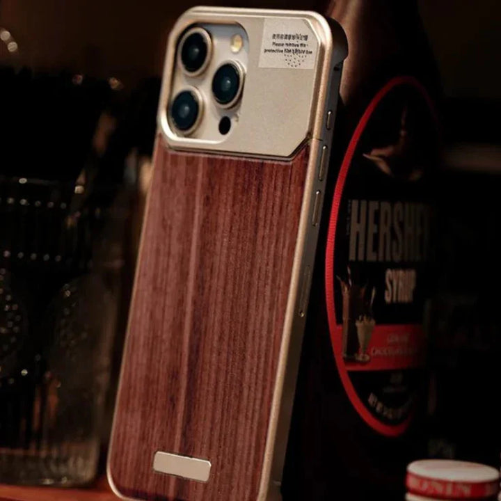 A smartphone with a stylish wood phone case stands upright on a surface. In the background, there is a bottle of Hershey’s chocolate syrup and a glass container with utensils.