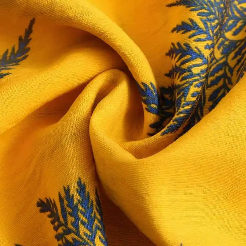 Close-up of yellow cotton shirt fabric with blue leaf or fern patterns, showing a swirl in the material that highlights its texture and classic design—perfect for a casual brunch.