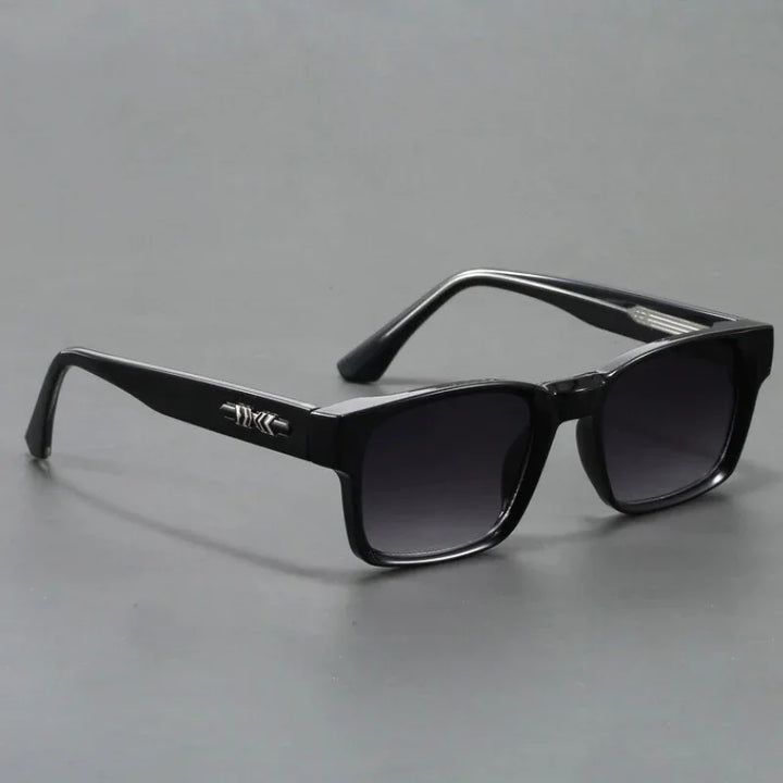 A pair of black rectangular sunglasses with modern design, featuring dark lenses and a silver decorative detail on the arms, displayed on a plain gray surface.
