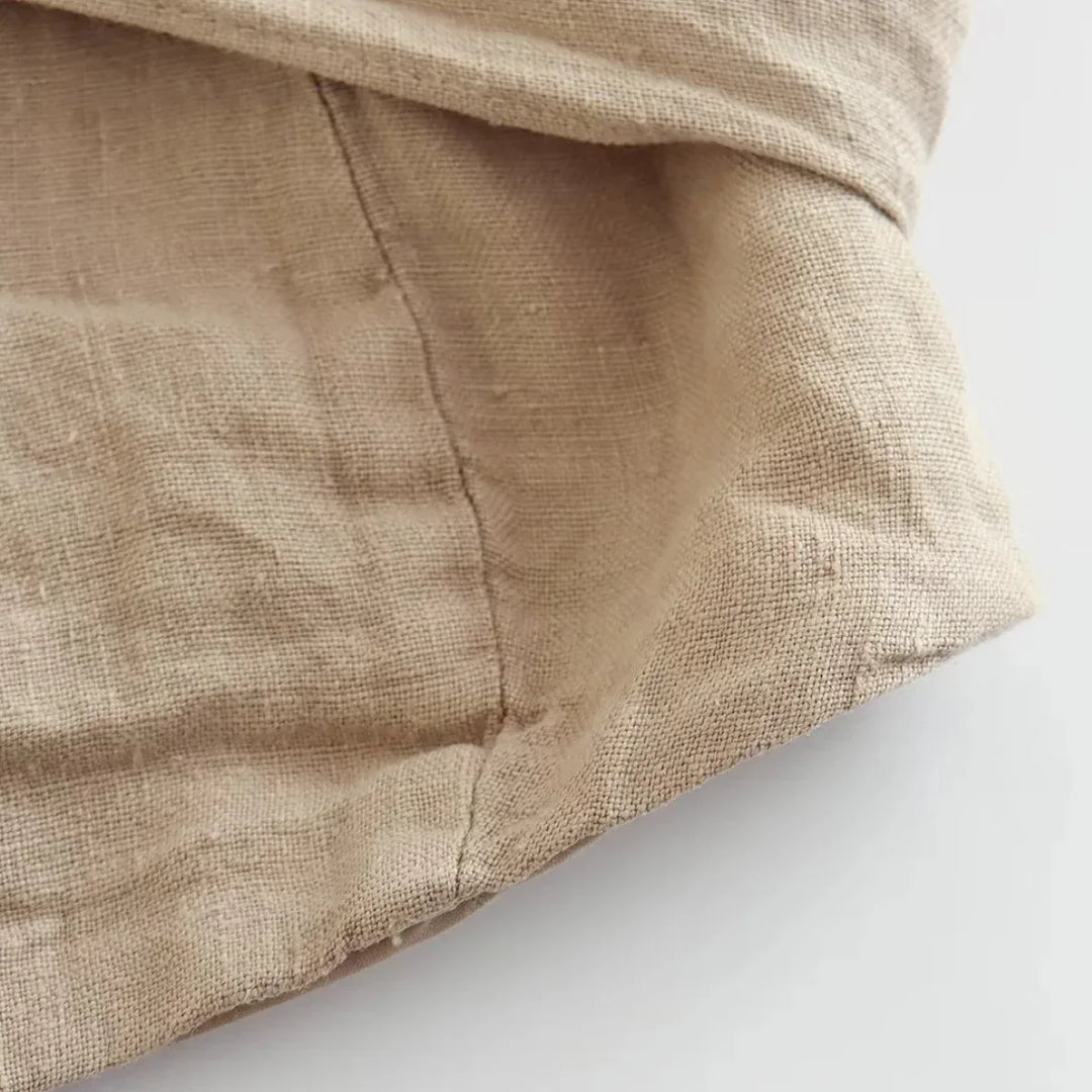 Close-up of a beige linen fabric with visible stitching and natural texture, ideal for wide-leg pants that capture effortless summer style, showing a seam and folded edge on a light background.