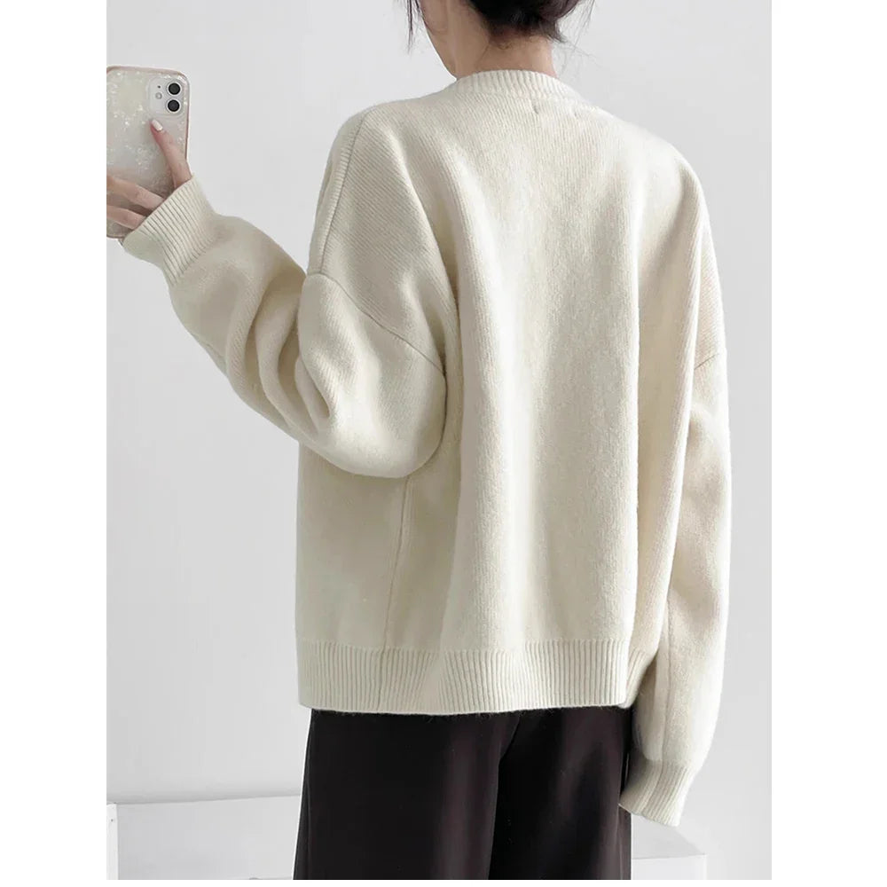 Woman wearing cream knit sweater and black pants, taking mirror selfie, Rovelli fashion