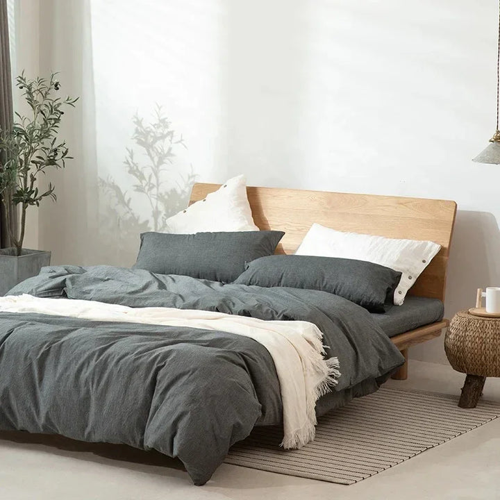Modern bedroom with wooden bed frame, grey bedding, white pillows, and minimalist decor
