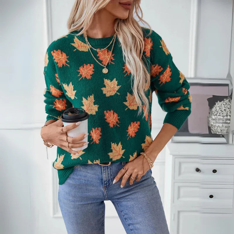 Woman wearing a comfortable green sweater with a soft knit material and subtle maple leaf pattern, blue jeans, and layered necklaces, holding a to-go coffee cup in a bright room with white furniture in the background.