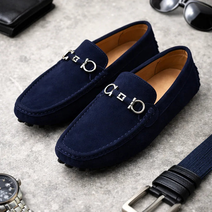 Rovelli blue suede loafers with silver hardware on grey surface, belt and accessories nearby
