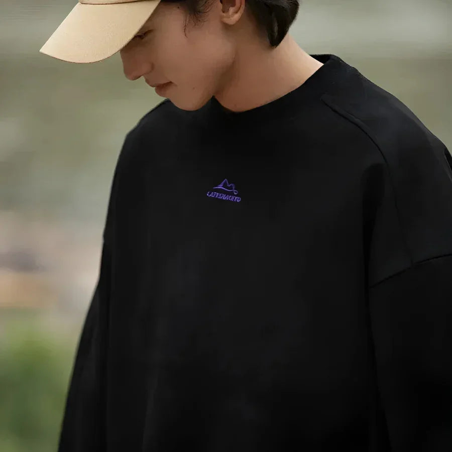 Man in beige cap and black Rovelli sweatshirt with purple mountain logo outdoors
