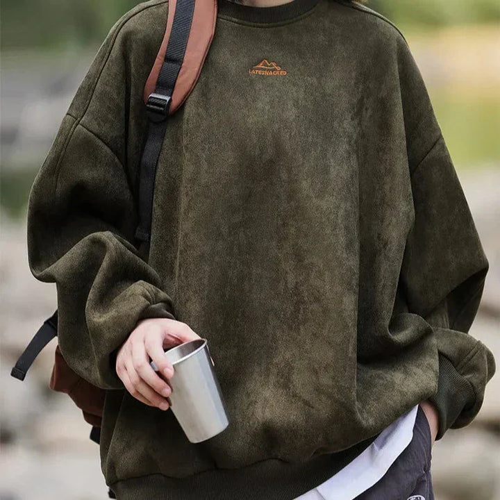 Person wearing olive green Rovelli sweatshirt outdoors, holding metal cup, with backpack