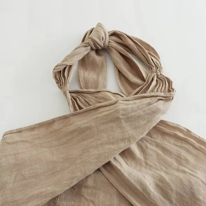 A beige, crinkled fabric bag with a twisted, knotted handle lies flat on a white surface—its soft, unstructured look and earthy texture make it a perfect accessory for summer style.