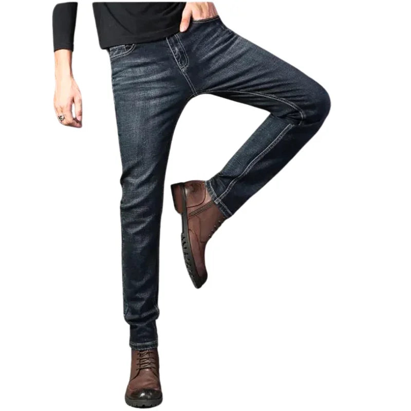 A person wearing dark blue slim-fit jeans, a black long-sleeve shirt, and brown lace-up boots poses with one leg bent and the other straight, against a white background.