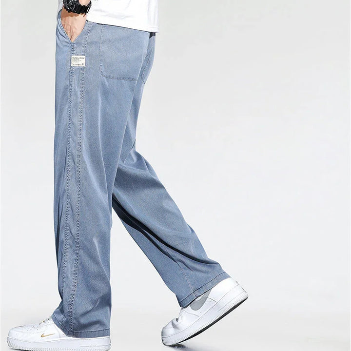 A person wearing Summer Loose Men Jeans in light blue and white Nike sneakers is shown walking, photographed from the waist down against a plain white background.