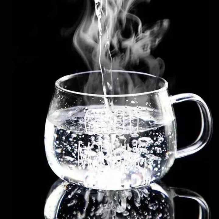 Clear heat-resistant glass mug on a black background with hot water being poured in, creating steam and bubbles inside the cup.