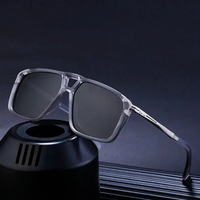 A pair of square, translucent gray polarized sunglasses with dark lenses is displayed, resting on a black cylindrical stand against a dark background.