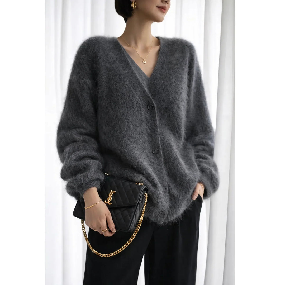 Woman wearing a fuzzy grey cardigan, black pants, and holding a black quilted handbag with gold chain