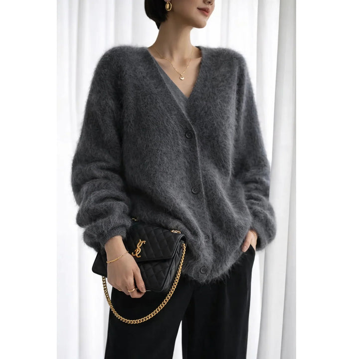 Woman wearing a fuzzy grey cardigan, black pants, and holding a black quilted handbag with gold chain