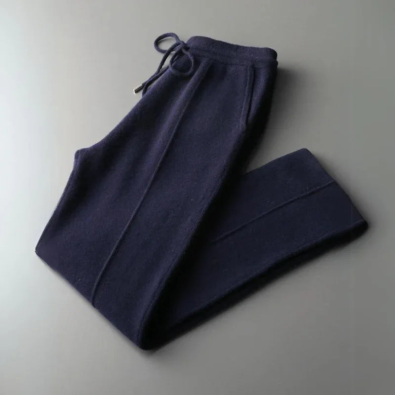 A pair of dark navy blue Merino wool pants with a drawstring waistband, neatly folded on a plain gray surface, offering comfortable pants with durable construction.