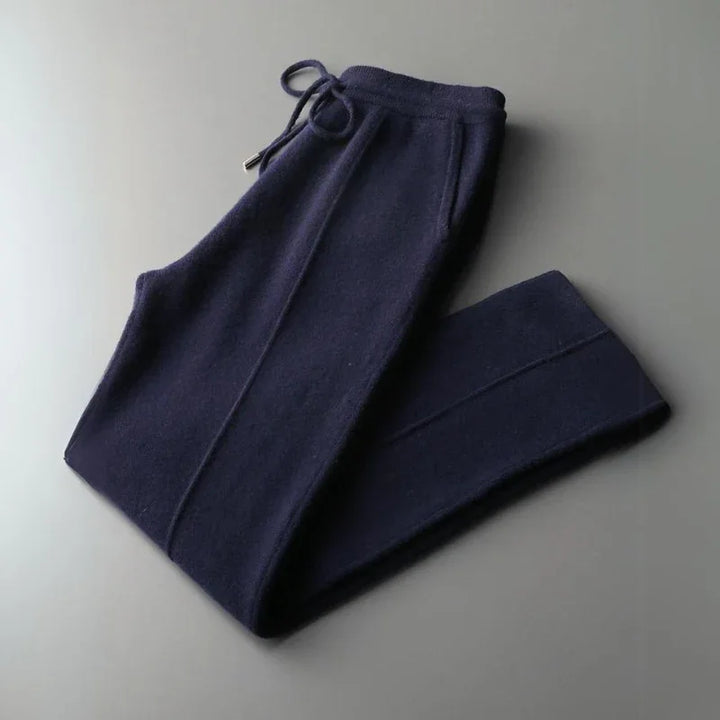 A pair of dark navy blue Merino wool pants with a drawstring waistband, neatly folded on a plain gray surface, offering comfortable pants with durable construction.