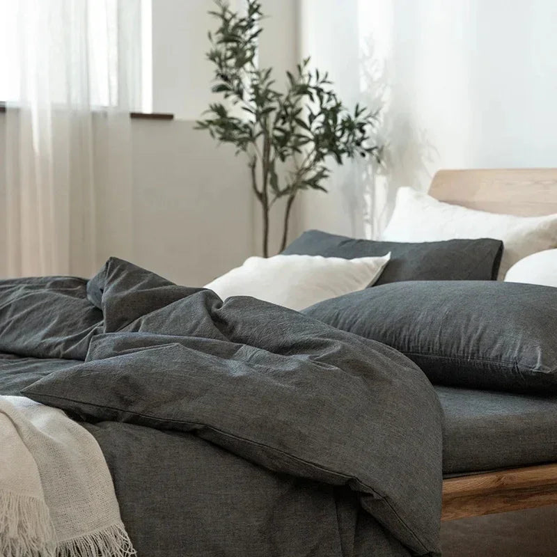 Modern bedroom with charcoal bedding, white pillows, wooden bed frame, and potted plant by Rovelli