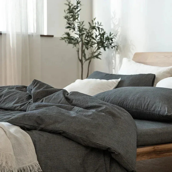 Modern bedroom with charcoal bedding, white pillows, wooden bed frame, and potted plant by Rovelli