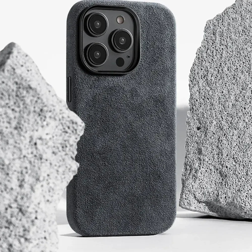 A smartphone with a suede finish, protective design case stands upright between two large, rough, light gray stones on a white background.