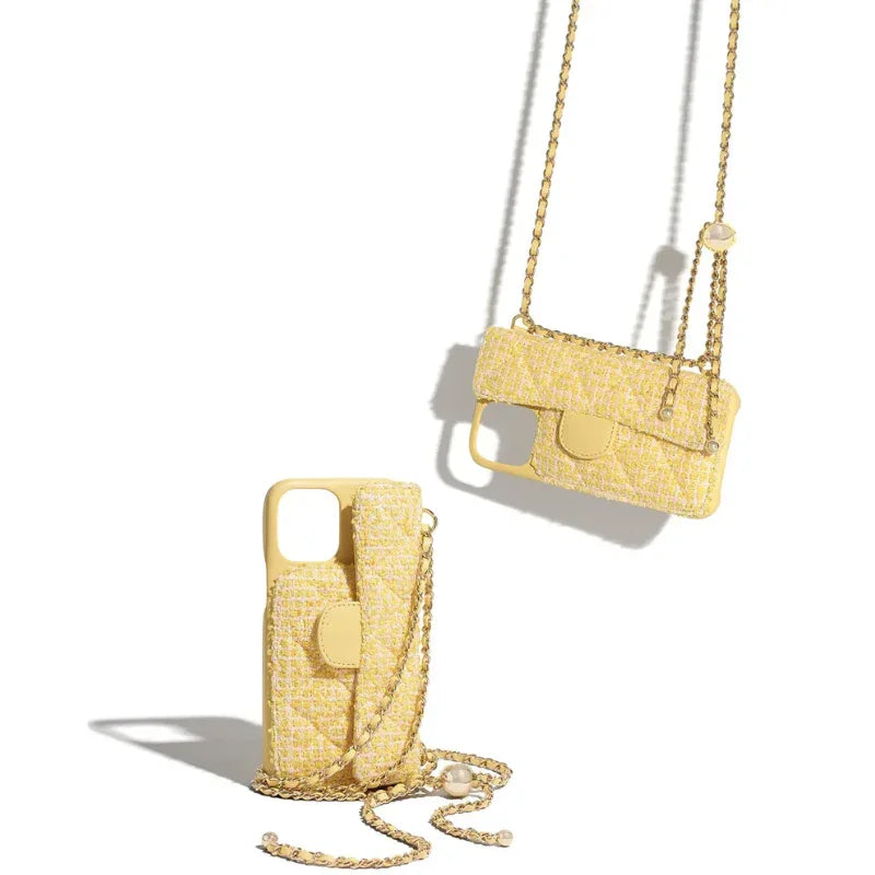Two yellow tweed-textured phone cases with a stylish chain strap are displayed against a white background, one standing upright and the other lying flat, casting soft shadows.