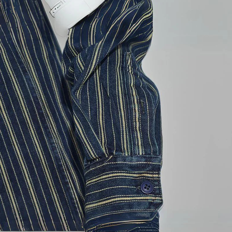A close-up of a relaxed-fit button-down navy shirt sleeve with thin yellow and white vertical stripes, showing a buttoned cuff. The sleeve is partially folded, and a white object is tucked under the arm.