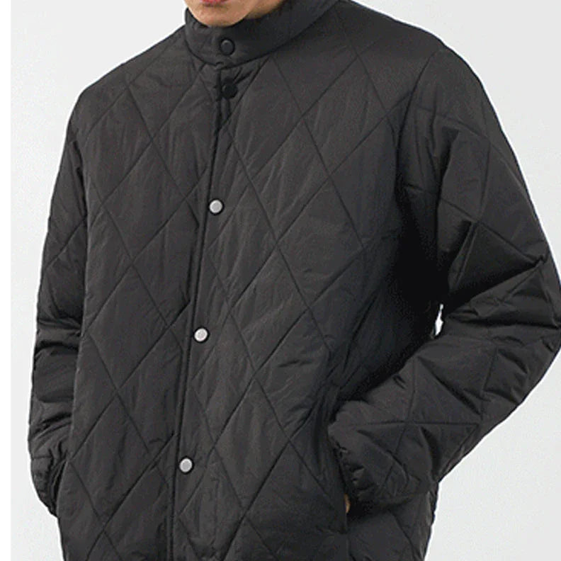 A person wearing a black, diamond-stitched pattern padded jacket with snap buttons stands against a plain light background. The lightweight insulating jacket features hands in pockets, and the head is partially out of frame.