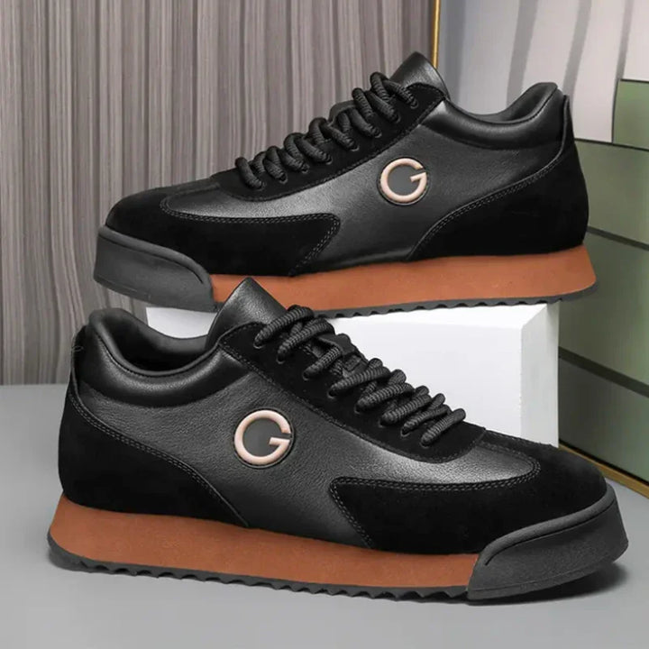 A pair of black sleek sneakers with brown soles, luxe leather suede accents, black laces, and a silver G logo on the side, displayed on a white box against a modern, striped background. Perfect for the urban professional.