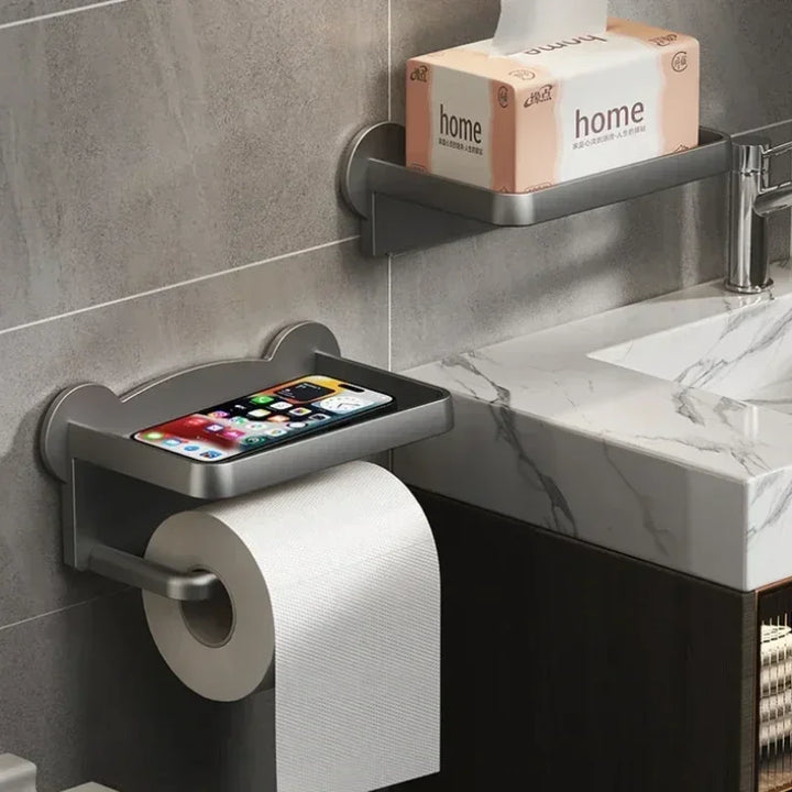 A moisture-resistant toilet paper holder with a built-in tray for your smartphone is mounted on the bathroom wall; above, a multi-functional shelf holds a tissue box beside a sink with a marble countertop.